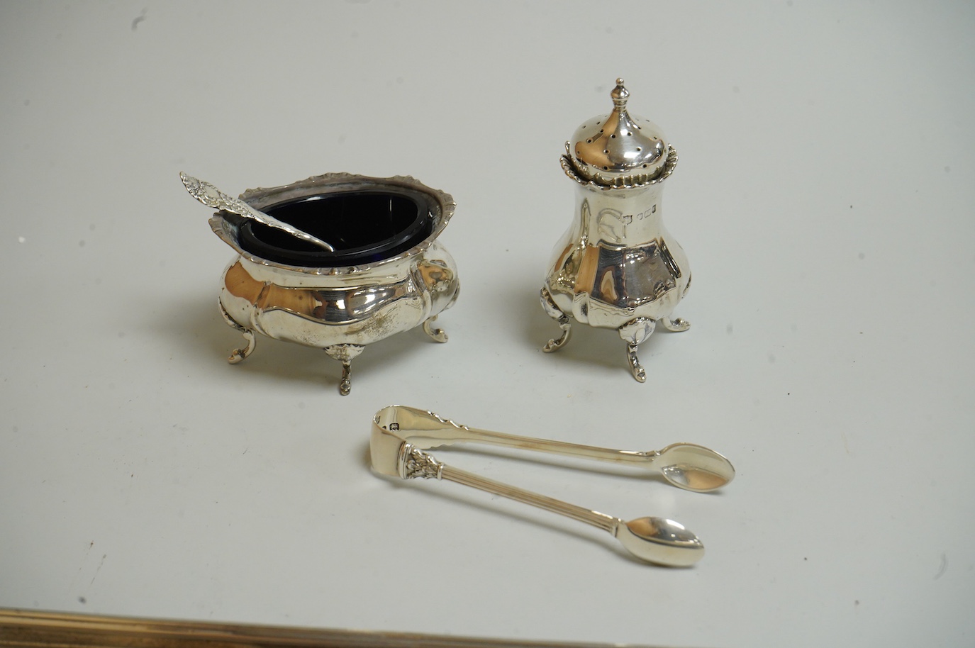 A George V silver sauceboat by Mappin & Webb, Birmingham, 1933, length 16.2cm, together with a silver salt and spoon, with blue glass liner, a silver pepperette, a pair of silver sugar tongs and a Spanish white metal two